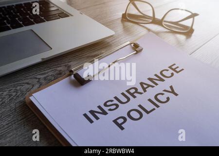 Paper clipboard with text INSURANCE POLICY on table with laptop and glasses. Stock Photo
