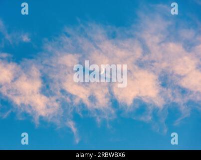 An evening sky with a waxing crescent moon showing through pink sunset clouds (UK) Stock Photo