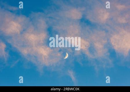 An evening sky with a waxing crescent moon showing through pink sunset clouds (UK) Stock Photo