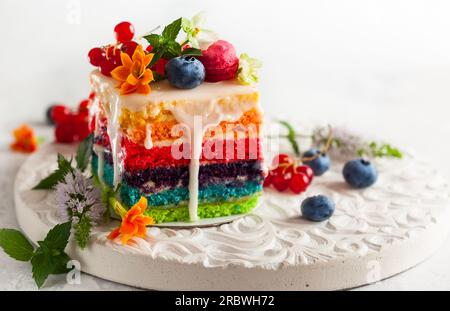 A slice of rainbow cake decorated with fresh berries and flowers for holiday Stock Photo