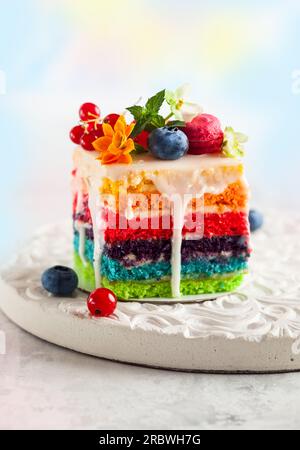 A slice of rainbow cake decorated with fresh berries and flowers for holiday Stock Photo