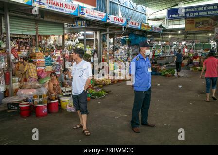 A uniformed security guard and a shopper stand facing away from each other next to stalls in Con Market, Danang, Vietnam. Stock Photo