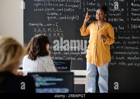 Teacher standing against the blackboard and teaching IT lesson to students at class Stock Photo