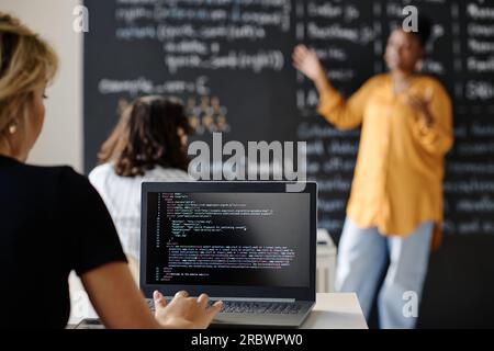 Rear view of student writing codes on laptop sitting at desk during IT lesson Stock Photo