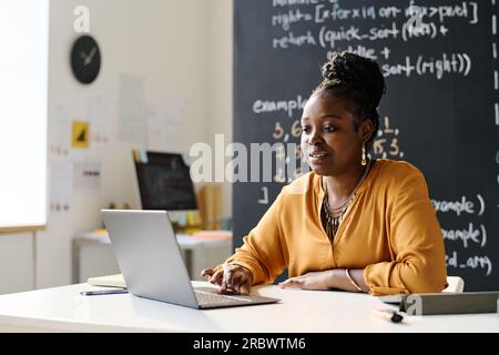 Young African American teacher working online on laptop while sitting in the classroom Stock Photo