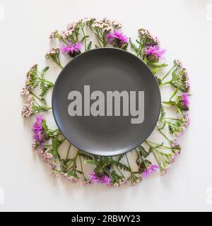 Wreath of wild purple and pink milk thistle on grey background. Flat lay. View from above. Space for text on black. Stock Photo
