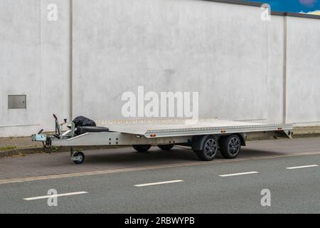 Side view of a platform car trailer standing on the side of the road along a concrete fence. Stock Photo
