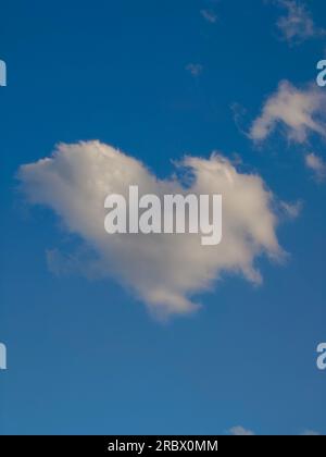 White puffy heart shaped cloud set against a deep blue summer sky Stock Photo