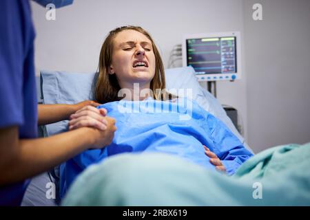 Pregnant woman, clinic and labor with push, holding hands or support in bed, baby and pain. Strong mother, childbirth process and helping hand in Stock Photo