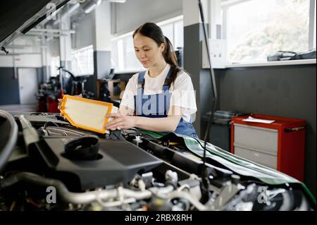 Female auto mechanic changing engine air filter in car Stock Photo