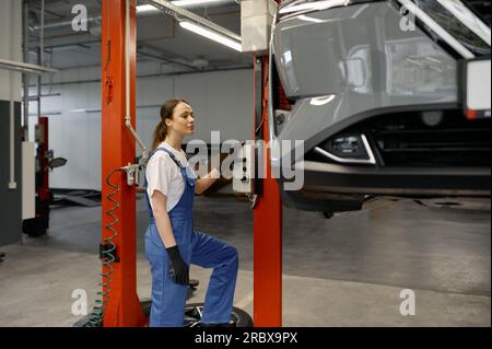 Young woman auto technician turning on car lift mechanism Stock Photo