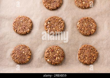 Raw halthy oatmeal cookies with dates, nuts and flaxseed on baking paper, top view. Cooking homemade vegan baking. Stock Photo