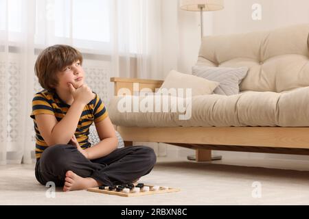 Playing checkers. Concentrated boy thinking about next move on floor in room Stock Photo