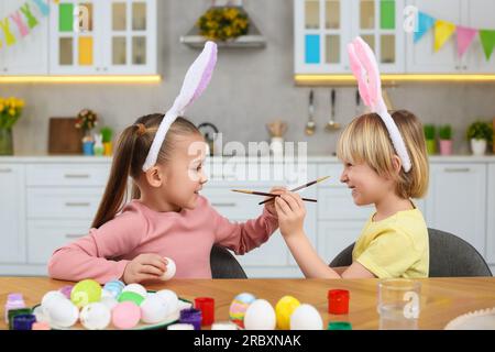 Children having fun while painting Easter eggs at table in kitchen Stock Photo