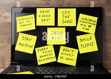 Paper notes of life-affirming phrases on laptop against wooden background Stock Photo