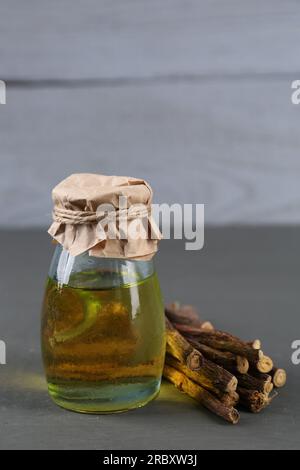 Dried sticks of licorice roots and essential oil on grey wooden table Stock Photo
