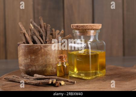 Dried sticks of licorice roots and essential oil on wooden board, closeup Stock Photo