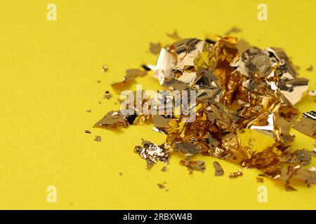 Many pieces of edible gold leaf on yellow background, closeup Stock Photo