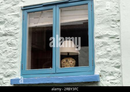 Study of a Blue Cottage Window with a Pretty Table Lamp on the Inside Window Ledge. Stock Photo