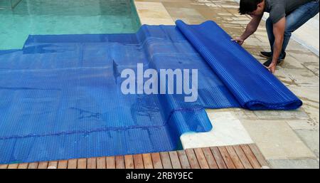 Man removing swimming pool cover and folding protector Stock Photo