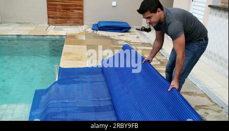 Man removing swimming pool cover and folding protector Stock Photo