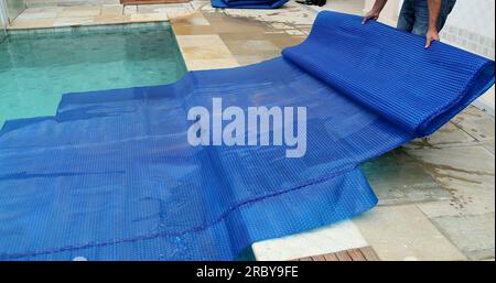 Man removing swimming pool cover and folding protector Stock Photo