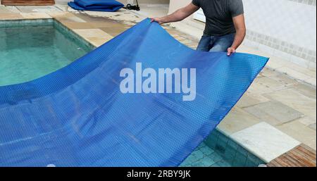 Man removing swimming pool cover and folding protector Stock Photo