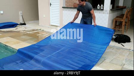 Man removing swimming pool cover and folding protector Stock Photo