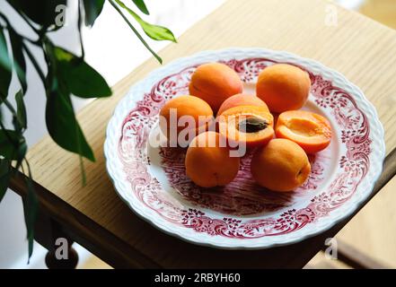 Fresh ripe apricots on plate on wooden table, sunny morning, village atmosphere, rustic. Cosy home interior. Harvest concept. Pile of whole juicy oran Stock Photo