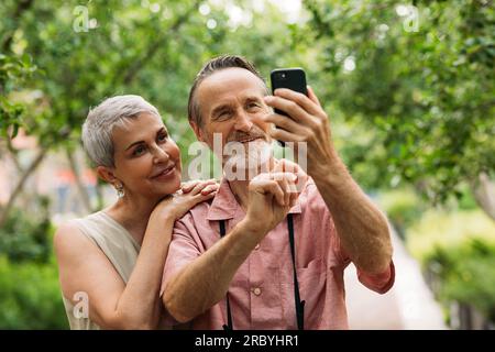 Aged smiling couple taking selfie outdoors in the park Stock Photo