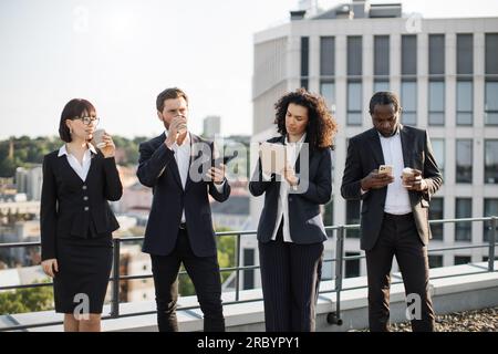 Group of young professionals taking short coffee break and enjoying hot beverage on fresh air. Multiracial coworkers having rest and discussing some working points concerning new business project. Stock Photo
