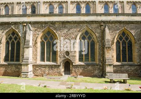 Part of Llandaff Cathedral facing south showing two layers of windows, a small 'side door' and a bench - all enjoying the sun. Stock Photo