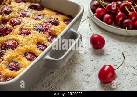 Clafoutis cherry tart - traditional french pie in a baking dish and fresh cherries on the gray table Stock Photo