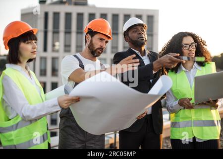 Diverse group of architects looking at construction diagram and discussing settlement of terraces on residential complex. African american woman holdi Stock Photo