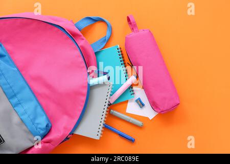 Pink school backpack with pencil case, notebooks and markers on orange background Stock Photo