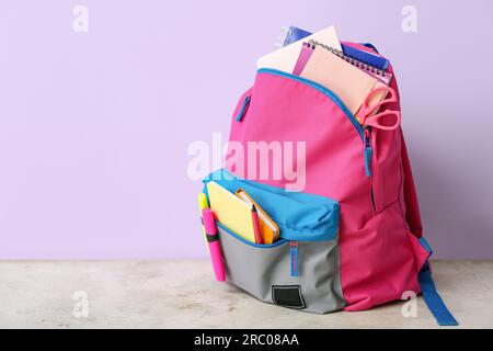 Color school backpack with notebooks, markers and scissors on light grunge table near lilac wall Stock Photo