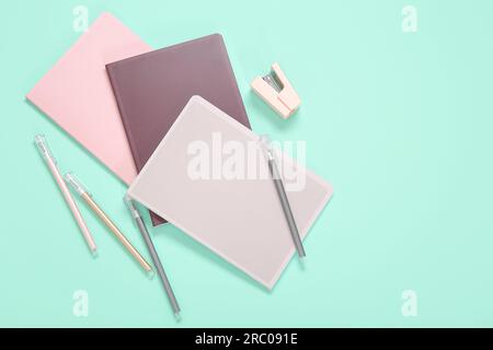 Different colorful notebooks with pens and stapler on turquoise background Stock Photo