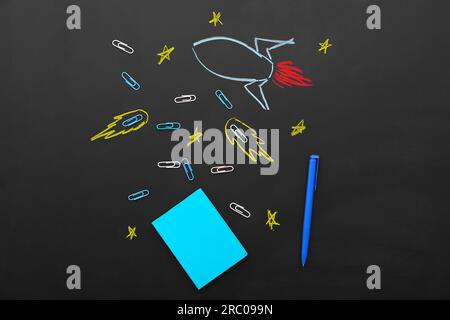 Creative composition with drawn rocket and different stationery on black chalkboard Stock Photo