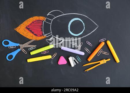 Creative composition with drawn rocket and different stationery on black chalkboard Stock Photo
