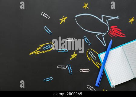 Creative composition with drawn rocket and different stationery on black chalkboard Stock Photo