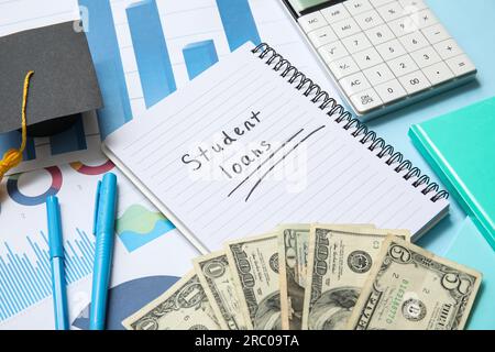 Notebook with text STUDENT LOANS, calculator, graduation cap, charts and dollar banknotes on blue background Stock Photo