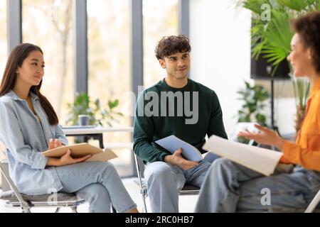 Happy international university students having a group discussion sitting together in circle of chairs and talking Stock Photo