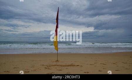 Single surf life saving flag on an empty sandy beach on a stormy day in Sunshine Beach, Queensland Stock Photo