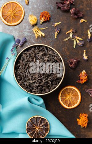 Composition of black, green, flower tea and dried orange slices on blue and brown backgrounds top view. Large-leaf tea, dried flowers and citrus chips Stock Photo