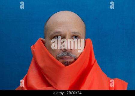 Bald, bearded man wearing an orange cloth around his neck. Isolated on blue background. Stock Photo