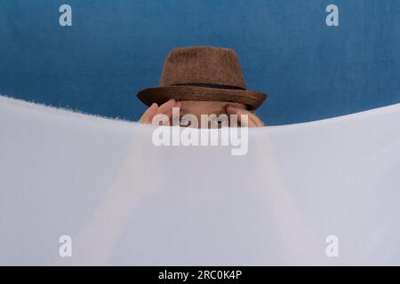Man wearing hat behind white colored cloth. isolated on blue background. Stock Photo