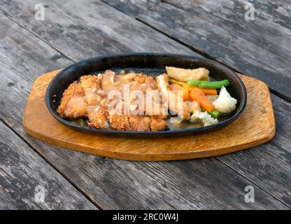 Sliced fried chicken at the hot plate, with vegetables, on an old vintage wooden table Stock Photo