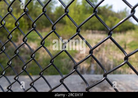 Black metal fence - green brown field in background - blurred background. Taken in Toronto, Canada. Stock Photo