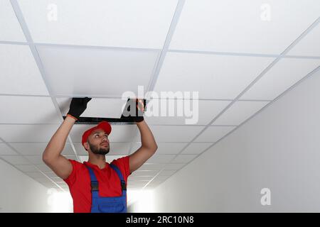 Electrician with pliers repairing ceiling light indoors, space for text Stock Photo