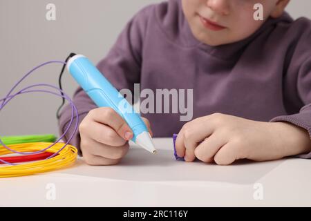 Boy drawing with stylish 3D pen at white table, closeup Stock Photo